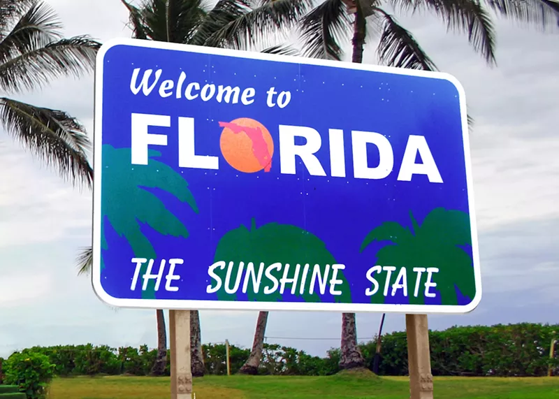 Image: A royal blue "Welcome to Florida, The Sunshine State" sign surrounded by palm trees.