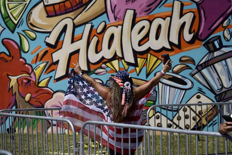 Image: A woman draped in an American flag stands in front of graffiti