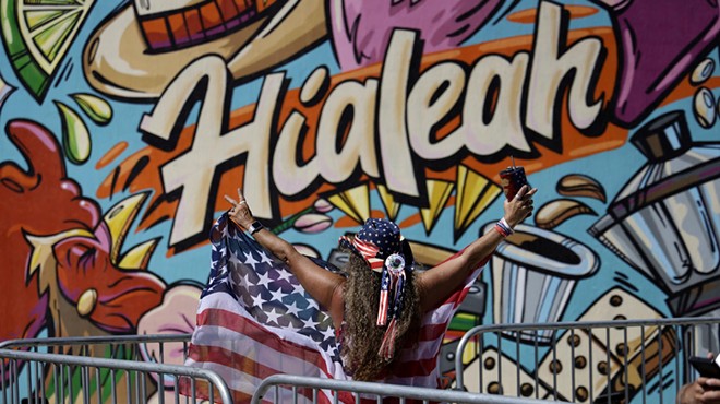 A woman draped in an American flag stands in front of graffiti