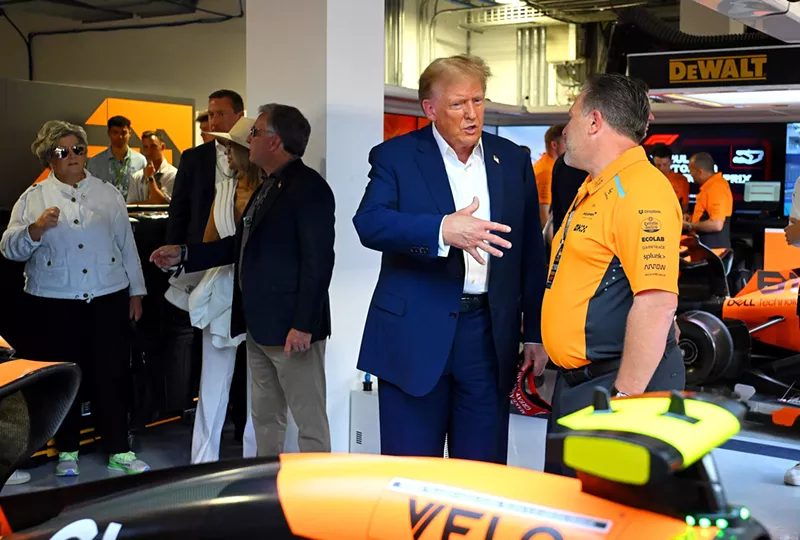 Image: Donald Trump stands in front of a race car, talking to a McLaren executive while gesturing with his right hand