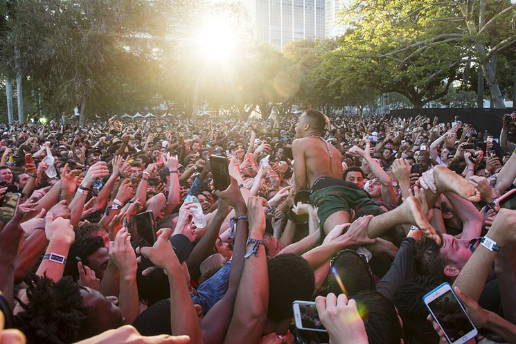 A color photo showing a barefoot Miami rapper XXXtentacion in the foreground of an enormous cluster of fans holding smartphones as he crowd-surfs at the 2017 Rolling Loud hip-hop festival at Bayfront Park in downtown Miami.