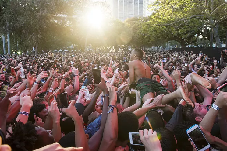 A color photo showing a barefoot Miami rapper XXXtentacion in the foreground of an enormous cluster of fans holding smartphones as he crowd-surfs at the 2017 Rolling Loud hip-hop festival at Bayfront Park in downtown Miami.