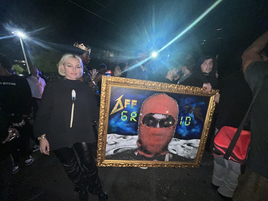 Two fans holding up a frame artwork of Kanye West in a red balaclava ski mask