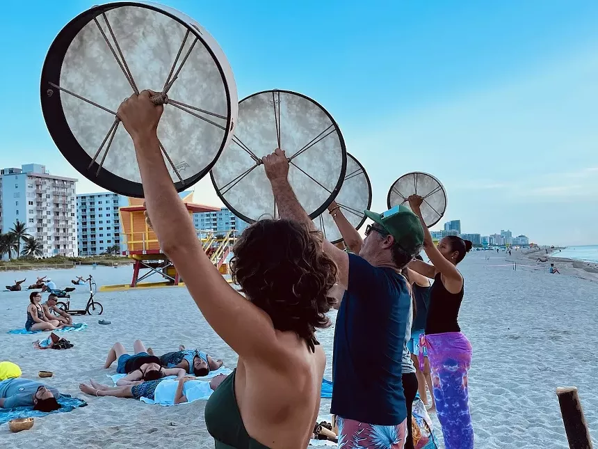 Musicians hold drums in the air as they stand on the beach