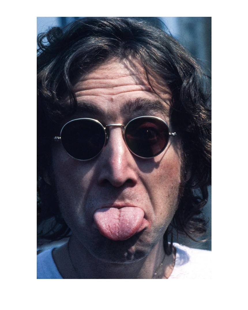 Color photo of John Lennon in sunglasses, sticking his tongue out in jest