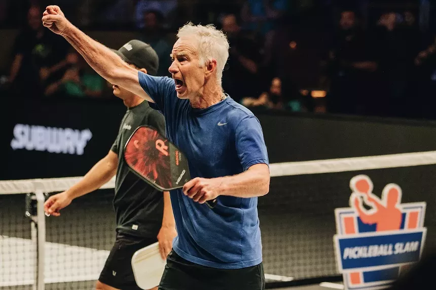 John McEnroe hold a racquet in his hand while celebrating