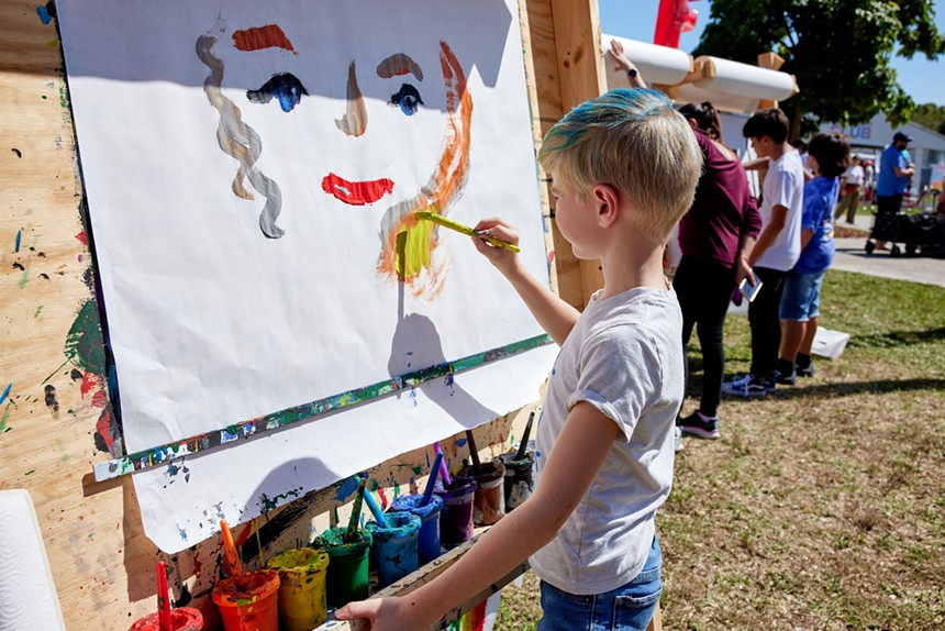 A young boy painting a face on a big sheet of paper
