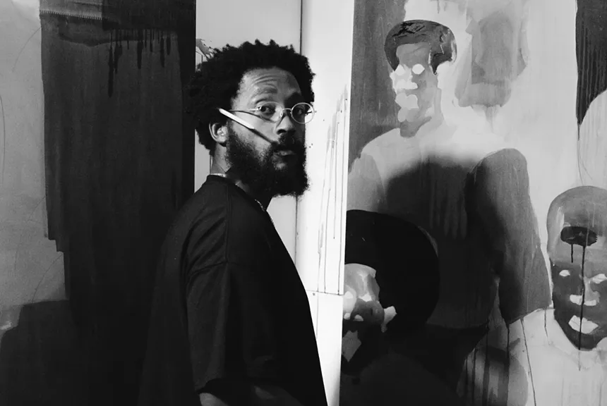 Black and white photo of Mark Delmont standing in front of a painted canvas