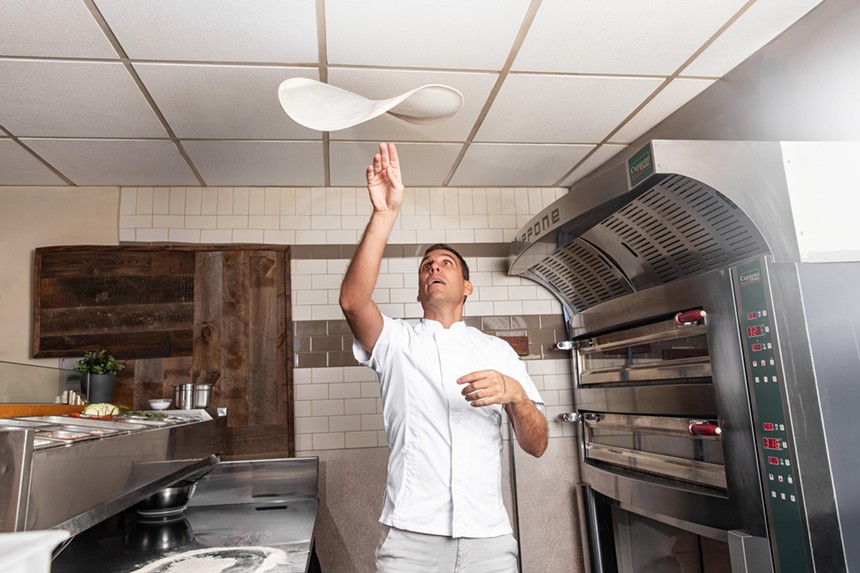 color photo of a pizza chef tossing pizza dough