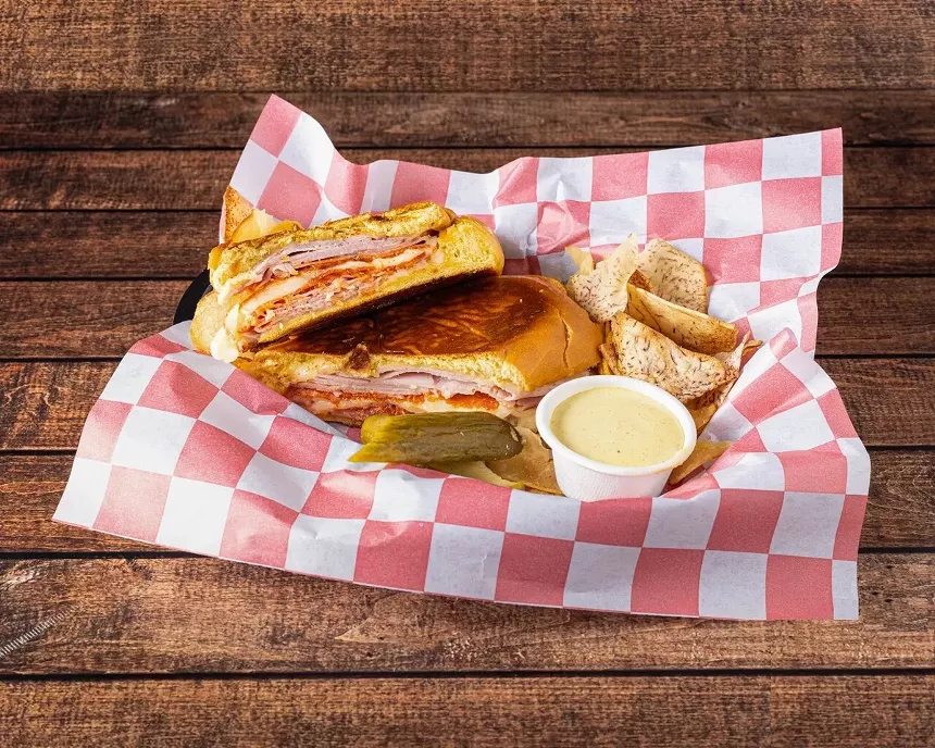 A panini sandwich with mustard sauce on the side served on wax red and white paper