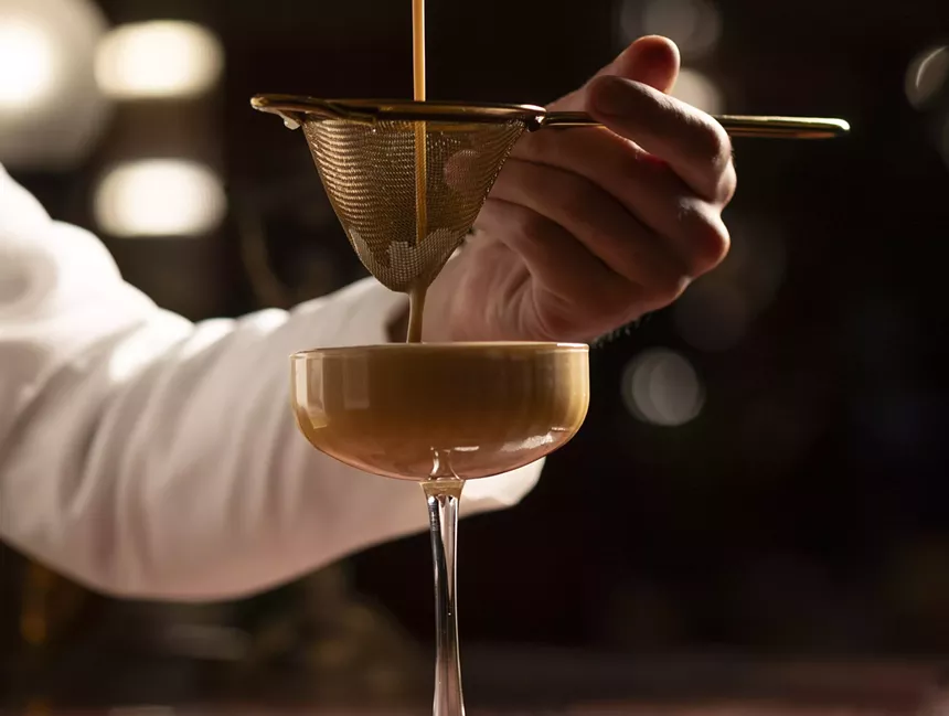 A person straining coffee through a colander