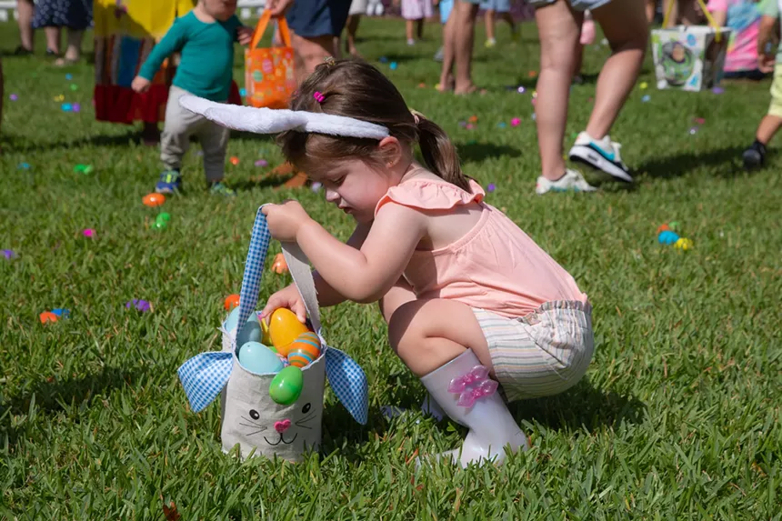 A young child filling her basket with Easter eggs