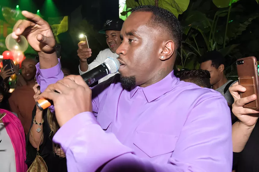 Closeup of rapper Sean "Diddy" Combs holding a microphone to his lips, surrounded by a crowd holding out their phone cameras