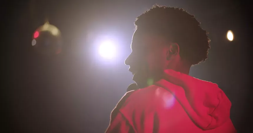 A spotlight hits a man in a red hoodie