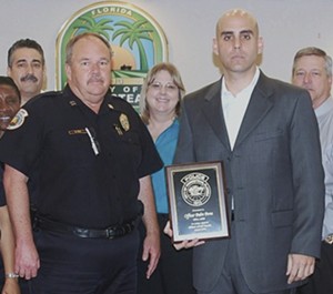 A South Florida police officer poses with fellow cops, wearing in a suit and holding an "Officer of the Month" award