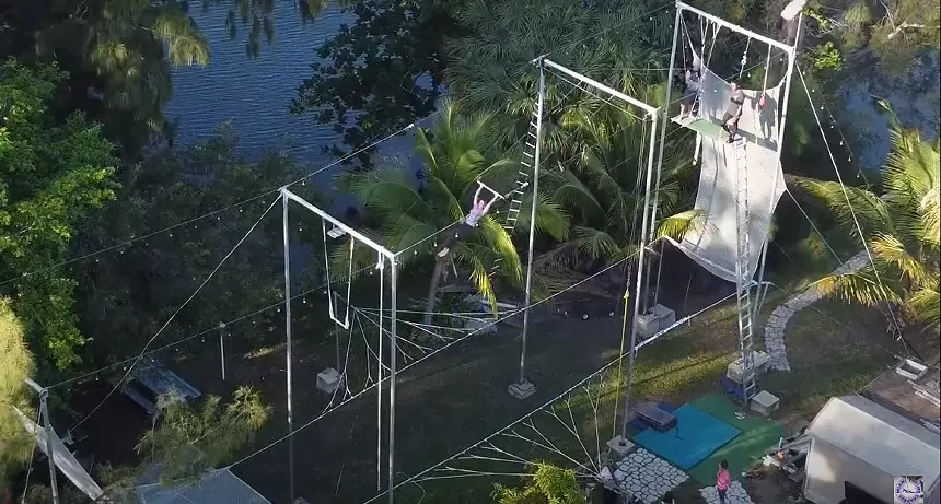A trapeze artist swings in the air in a modular trapeze rig set up in a Miami man's backyard