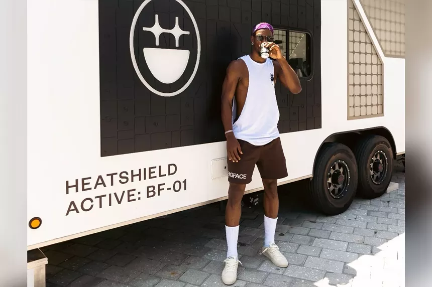A basketball star wearing shorts and a tank top and sipping coffee from a cup in front of a truck