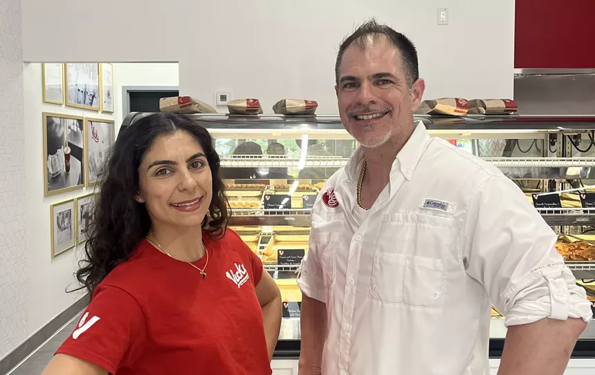 Two people posing in front of glass case of pastries