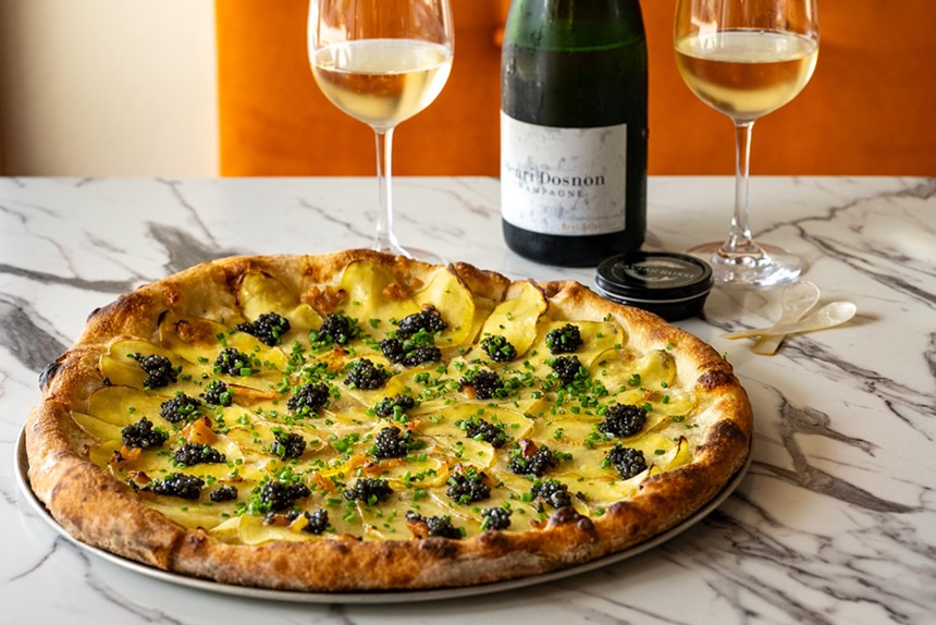 A pizza covered in black caviar next to a glass of white wine on a table