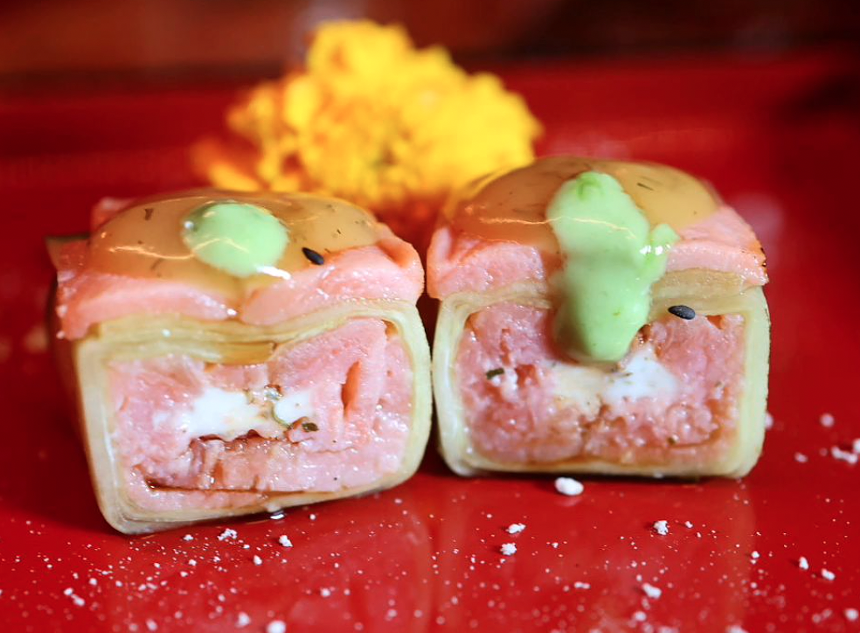 two sushi rolls with toppings and sauce on a red plate