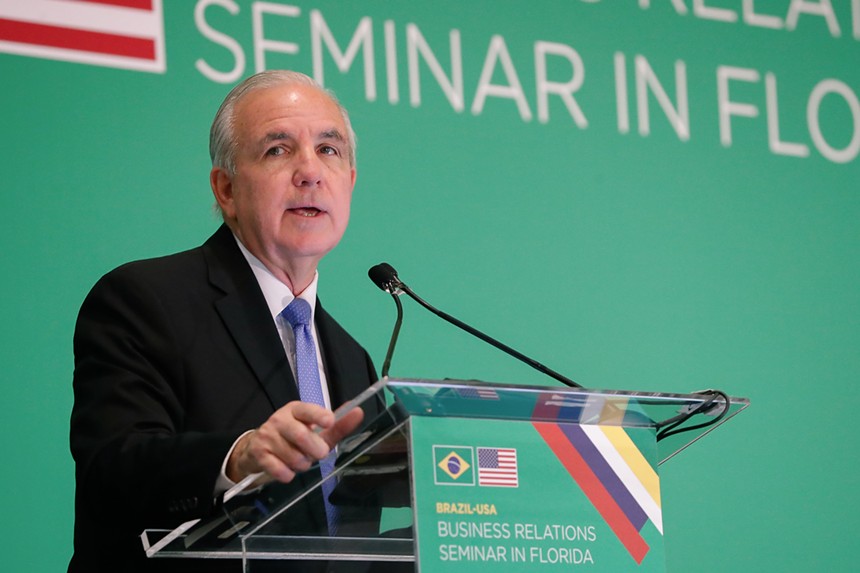 Congressman Carlos Giménez speaks at a podium with a blank green background