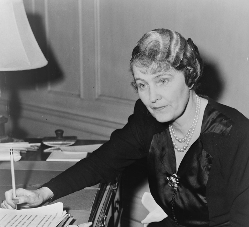 Archival black-and-white photo of Marjorie Merriweather Post seated with a pencil in hand at desk
