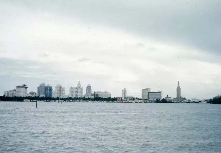 bluish tinted color photo of the miami skyline with the slightly choppy waters of biscayne bay in the foreground.