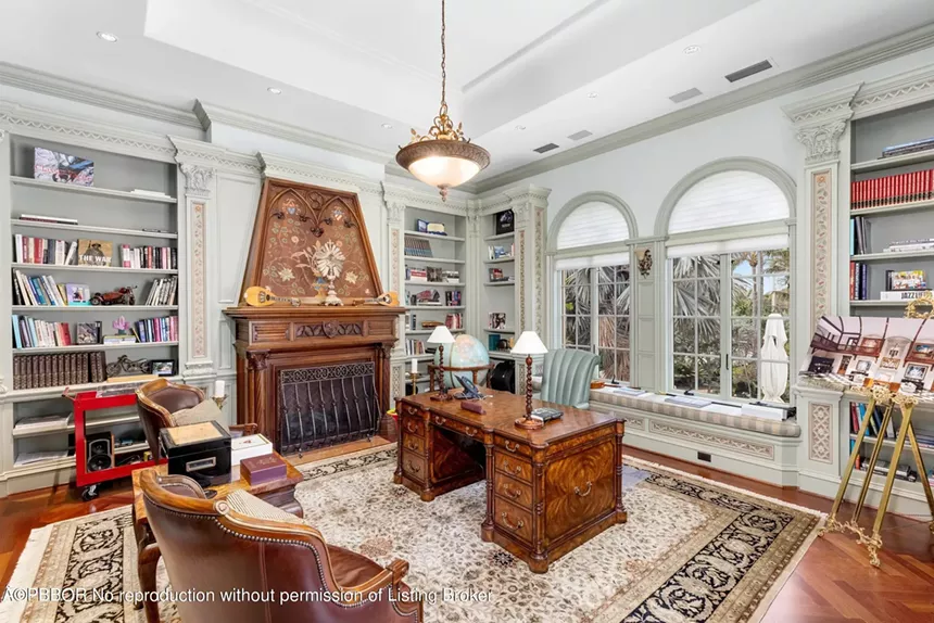 Custom wood-paneled office with a fireplace, built-in shelves, and natural light from large windows
