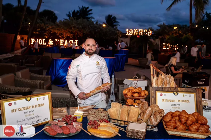 a man in a chef outfit standing by a table spread of bread