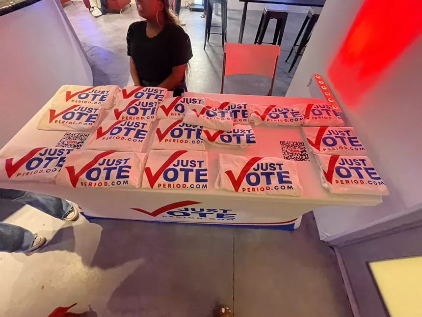Table with Just Vote Period T-shirts with QR codes beside them at the watch party