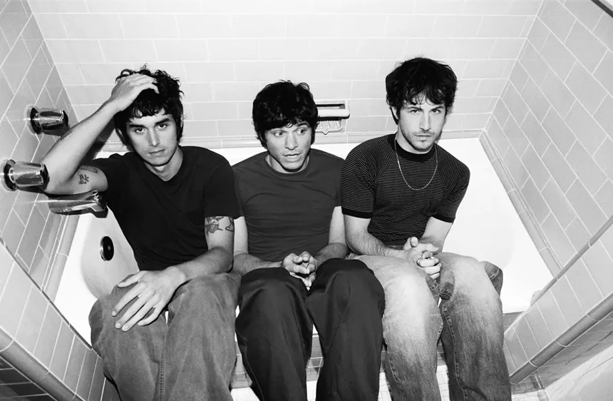 black and white photo of three men in a bathtub wearing black t-shirts and jeans