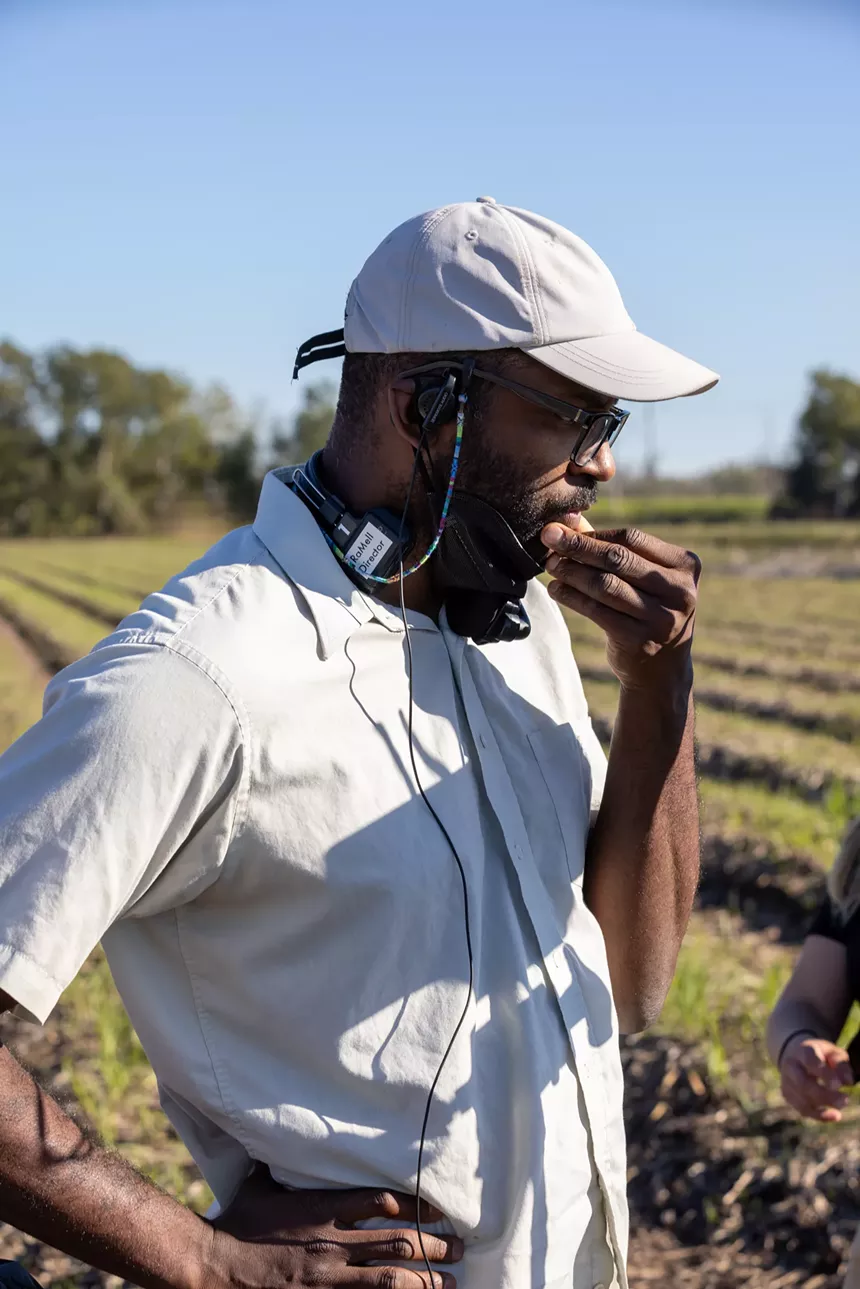 A man in a baseball cap and button-down shirt lost in thought. He's wearing a headset. A sticker on it reads, "RaMell Director"