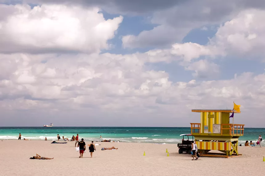 people walk on the beach next to a colorful lifeguard stand