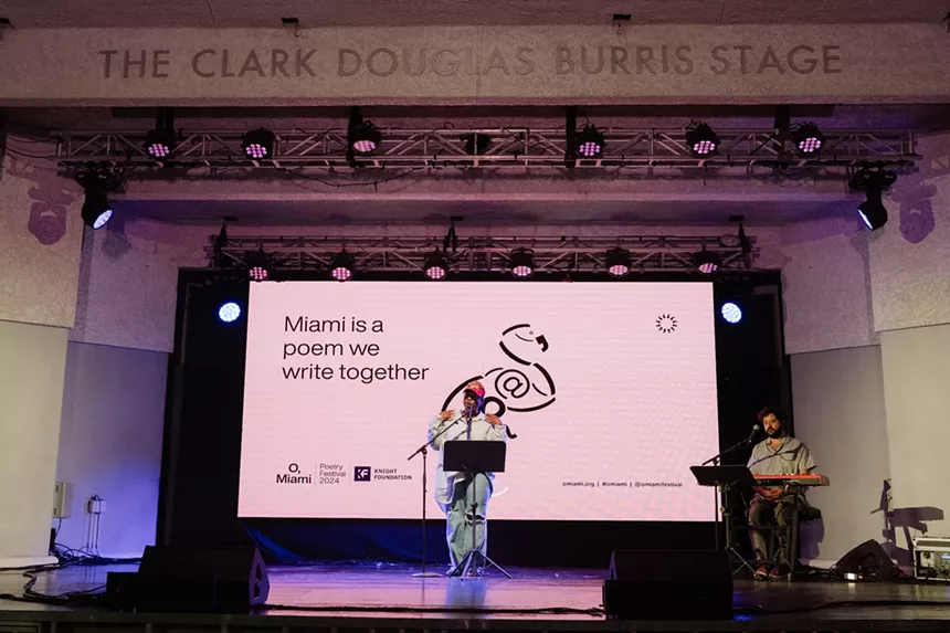 a person performs at a microphone on stage while a man plays keyboard behind them