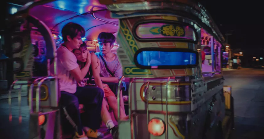 three young men hug inside a colorful bus with its interior lit in lavender