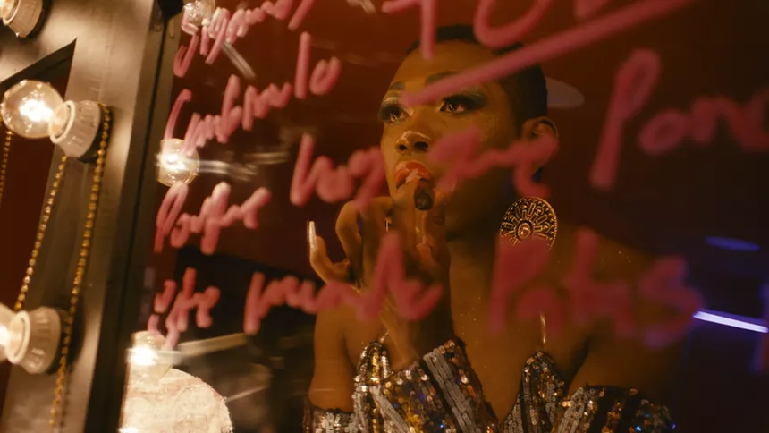 a Black drag queen applies lipstick at a mirror