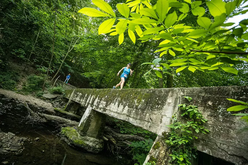 a woman runs through a park on a pedestrian bridge covered in moss