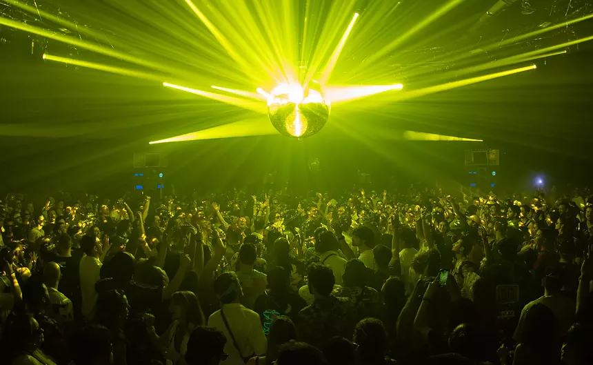 photo of a crowd bathed in yellow-green laser light with a large disco ball at the center