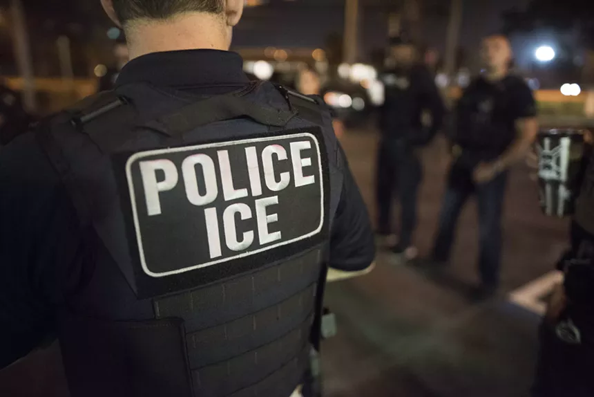 The back of an ICE agent wearing a bulletproof vest that reads, "POLICE ICE."