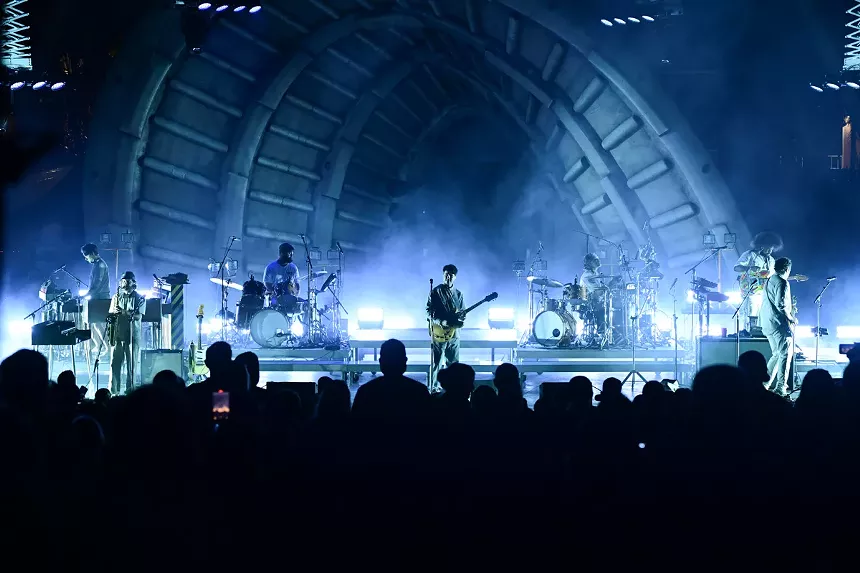 a band performing on an amphitheater stage under eerie, cloudy lighting