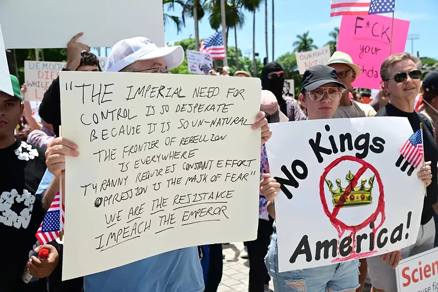 Protesters hold up signs reading, "The imperial need for control is so desperate because it is so unnatural/The frontier of rebellion is everywhere/Tyranny requires constant effort/Oppression is the mask of fear/We are the resistance/Impeach the emperor," and "No Kings America"