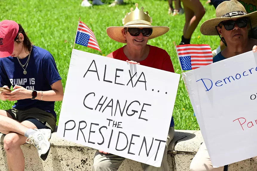 A protester holds a sign reading, "Alexa...Change the President."