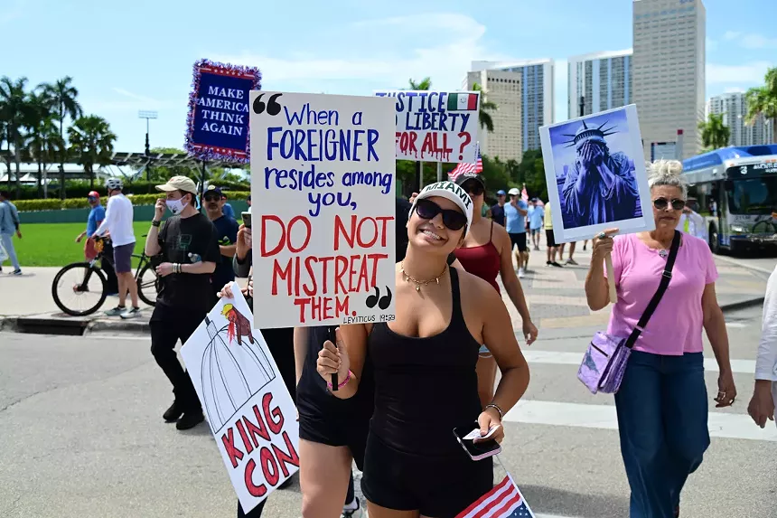 Protesters hold signs reading, "Make America Think Again," "King Con," "Justice and Liberty for All?" and "When a foreigner resides among you, do not mistreat them. Leviticus 19:33"