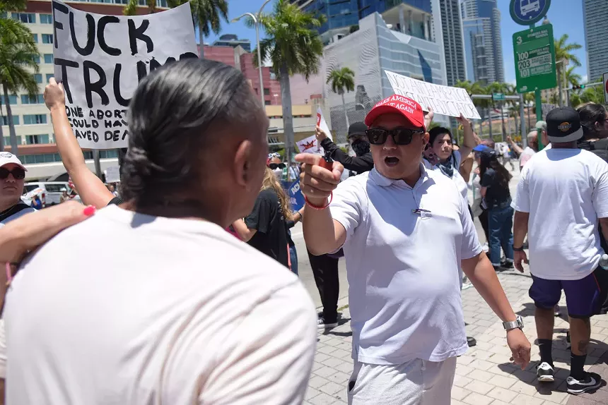 A man in a "MAGA" hat points at a rally-goer.