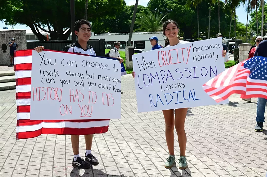Two young protesters hold signs and demonstrate against President Donald Trump.