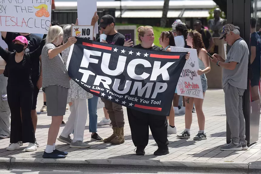 Protesters hold a "Fuck Trump" flag.