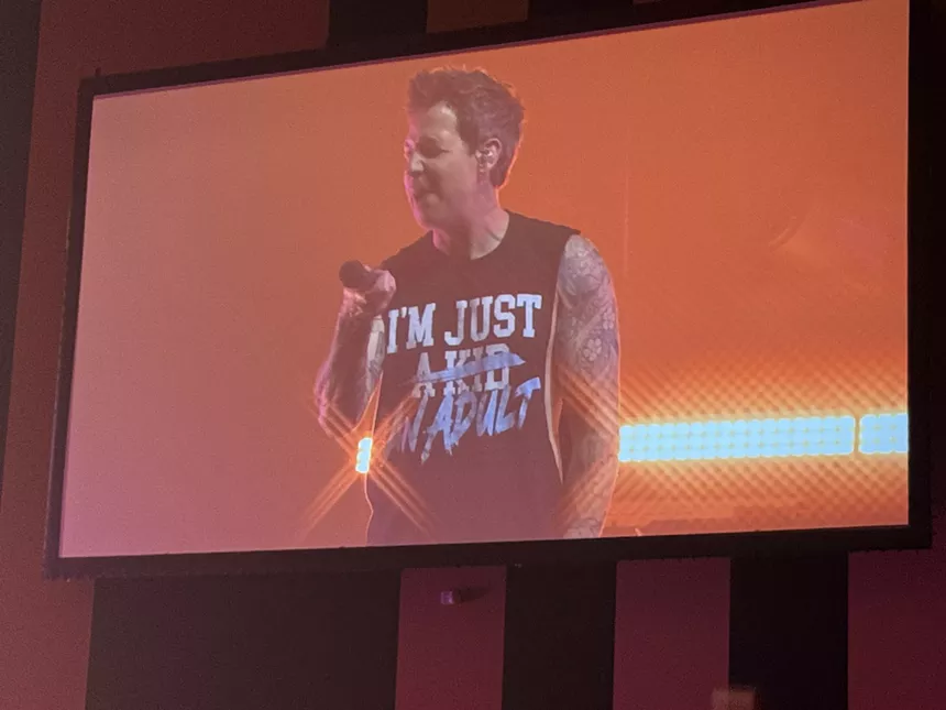 a concert Jumbotron shows Simple Plan singer Pierre Bouvier wearing a t-shirt reading, "I'm Just a Kid." The words "A Kid" are crossed out and replaced with "an adult."