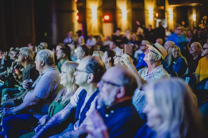 Man taking a picture with his phone during a concert at a theater.