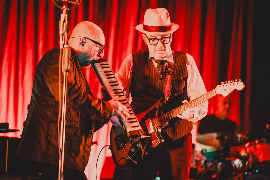 Man playing the melodica during a concert next to another man playing the guitar.