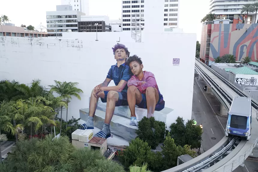 a mural on a white building shows two young boys sitting on a cinder block